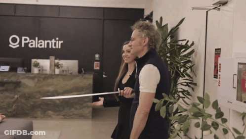 A Man And A Woman Are Standing In Front Of A Palantir Sign GIF