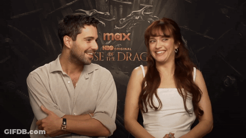 A Man And A Woman Are Standing In Front Of A Poster For Max Hbo Original GIF