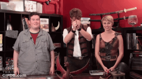 A Man And A Woman Are Standing In Front Of A Shelf With A Book Titled Saving Throw GIF