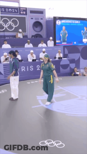 A Man And A Woman Are Standing In Front Of A Sign That Says ' Paris 2024 ' On It GIF