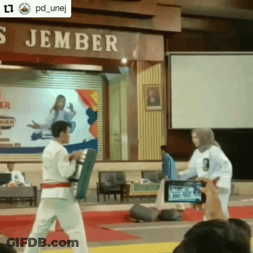 A Man And A Woman Are Standing In Front Of A Sign That Says ' S Jember ' On It GIF