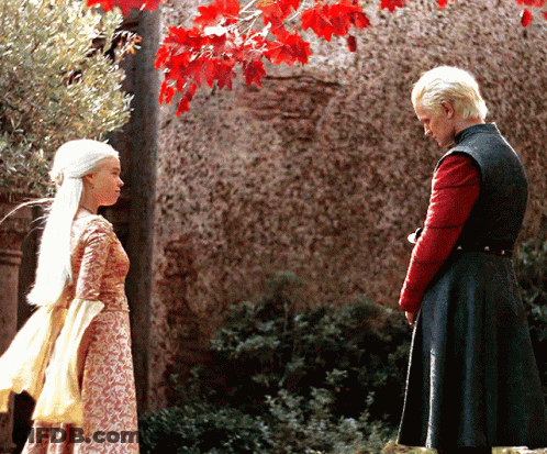 A Man And A Woman Are Standing In Front Of A Stone Wall GIF