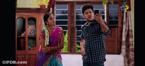 A Man And A Woman Are Standing In Front Of A Window . GIF