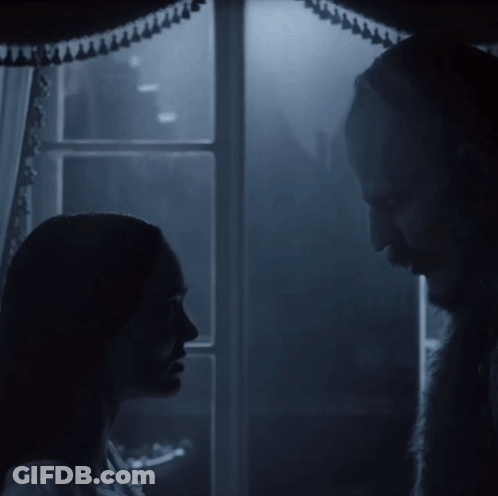 A Man And A Woman Are Standing In Front Of A Window GIF