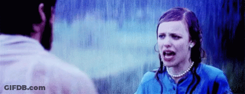 A Man And A Woman Are Standing In The Rain . The Woman Is Wearing A Pearl Necklace And A Blue Shirt . GIF