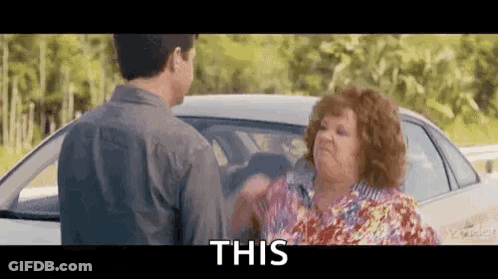 A Man And A Woman Are Standing Next To A Car And The Woman Is Holding The Man 'S Hand . GIF