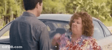 A Man And A Woman Are Standing Next To A Car . GIF