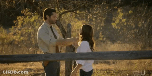 A Man And A Woman Are Standing Next To A Fence GIF