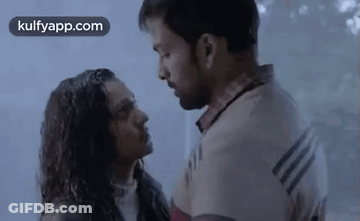 A Man And A Woman Are Standing Next To Each Other And Kissing In The Rain . GIF