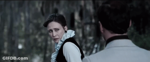 A Man And A Woman Are Standing Next To Each Other And Looking At Each Other In A Dark Room . GIF