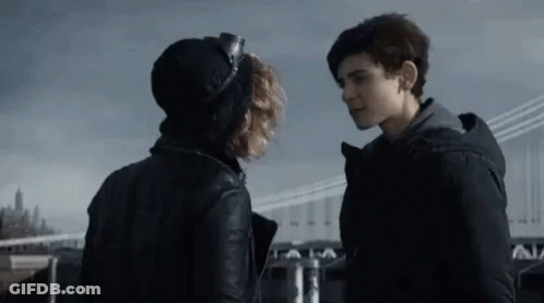 A Man And A Woman Are Standing Next To Each Other And Looking At Each Other In Front Of A Bridge . GIF