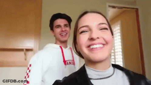 A Man And A Woman Are Standing Next To Each Other And Smiling . The Woman Is Wearing A Vans Sweatshirt . GIF
