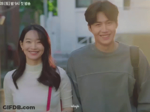 A Man And A Woman Are Standing Next To Each Other And The Woman Has A Pink Purse On Her Shoulder And The Man Is Smiling GIF