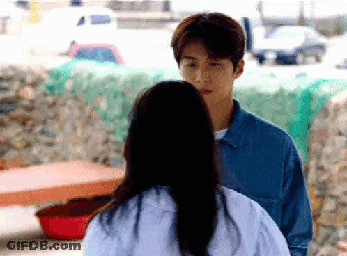 A Man And A Woman Are Standing Next To Each Other And The Woman Is Looking At The Man . GIF
