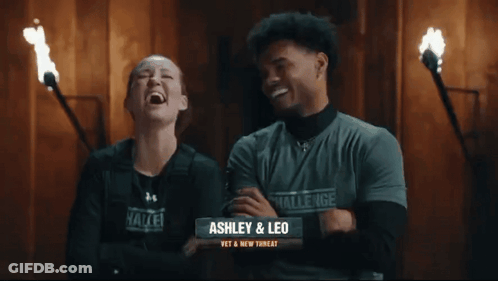 A Man And A Woman Are Standing Next To Each Other And The Woman Is Wearing A Challenge Shirt GIF
