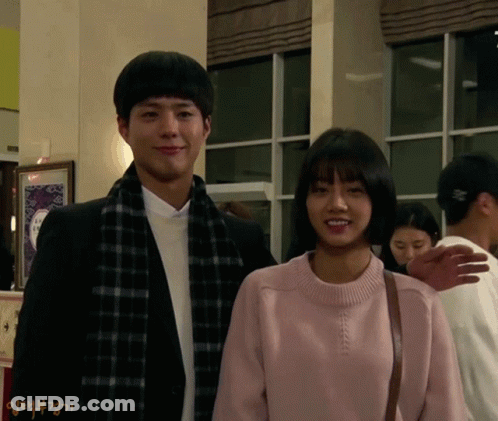 A Man And A Woman Are Standing Next To Each Other And The Woman Is Wearing A Pink Sweater And Scarf GIF