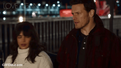 A Man And A Woman Are Standing Next To Each Other And The Words Love Again Are Visible In The Background GIF