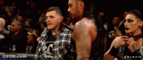 A Man And A Woman Are Standing Next To Each Other In A Crowd GIF