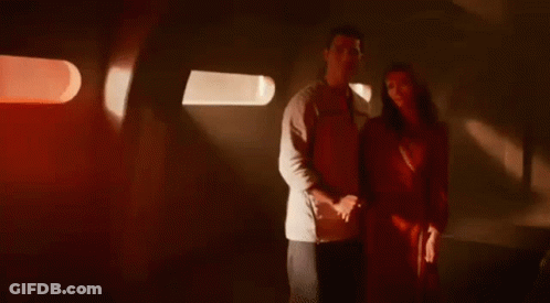 A Man And A Woman Are Standing Next To Each Other In A Dark Room Holding Hands . GIF