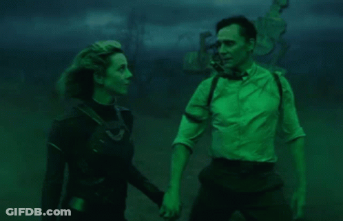 A Man And A Woman Are Standing Next To Each Other In A Dark Room Holding Hands . GIF