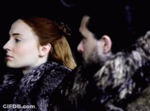 A Man And A Woman Are Standing Next To Each Other In A Dark Room . The Man Is Wearing A Fur Coat . GIF