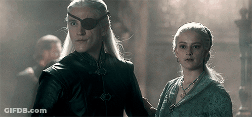 A Man And A Woman Are Standing Next To Each Other In A Dark Room . The Man Is Wearing An Eye Patch . GIF