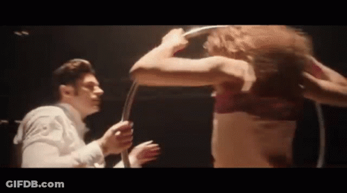 A Man And A Woman Are Standing Next To Each Other In A Dark Room . The Woman Is Wearing A Red Bra . GIF