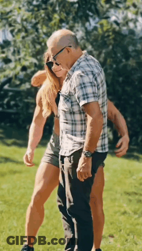 A Man And A Woman Are Standing Next To Each Other In A Grassy Field . GIF