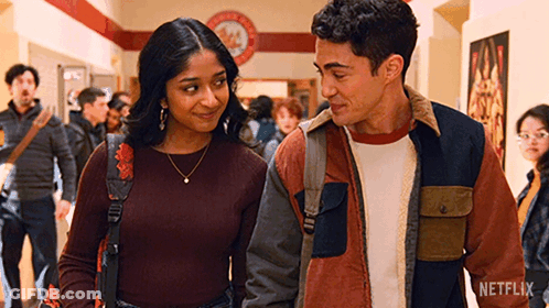 A Man And A Woman Are Standing Next To Each Other In A Hallway And Looking At Each Other . GIF