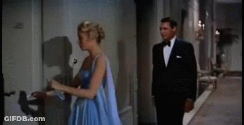 A Man And A Woman Are Standing Next To Each Other In A Hallway . The Woman Is Wearing A Blue Dress . GIF