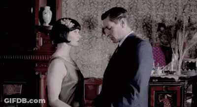 A Man And A Woman Are Standing Next To Each Other In A Living Room And Holding Hands . GIF