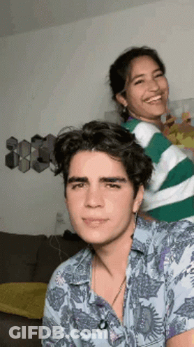 A Man And A Woman Are Standing Next To Each Other In A Living Room And Smiling . GIF