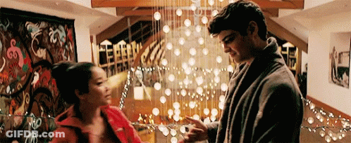 A Man And A Woman Are Standing Next To Each Other In A Living Room In Front Of A Christmas Tree . GIF