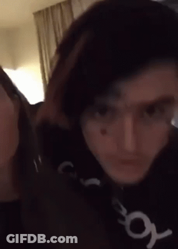 A Man And A Woman Are Standing Next To Each Other In A Room And Looking At The Camera . GIF