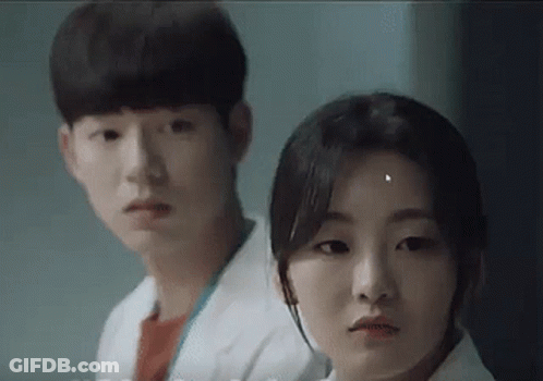 A Man And A Woman Are Standing Next To Each Other In A Room And Looking At The Camera . GIF