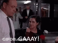 A Man And A Woman Are Standing Next To Each Other In A Room And The Woman Is Holding A Rose . GIF