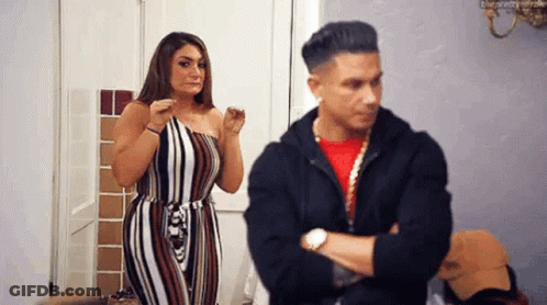 A Man And A Woman Are Standing Next To Each Other In A Room . The Man Is Looking At The Woman . GIF