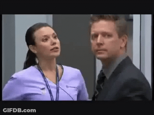 A Man And A Woman Are Standing Next To Each Other In A Room . The Man Is Wearing A Suit And Tie . GIF