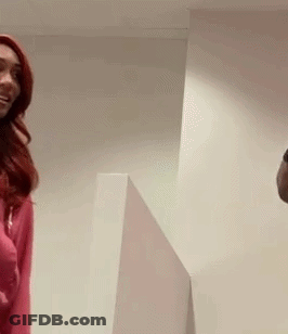 A Man And A Woman Are Standing Next To Each Other In A Room . The Woman Is Wearing A Pink Sweater . GIF