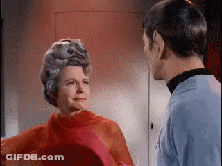 A Man And A Woman Are Standing Next To Each Other In A Room . The Woman Is Wearing A Red Dress . GIF