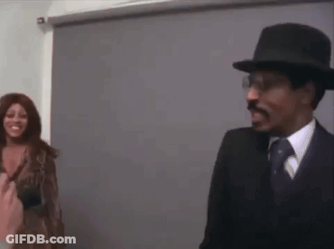 A Man And A Woman Are Standing Next To Each Other In A Room . The Woman Is Wearing A Wig . GIF