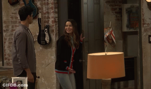 A Man And A Woman Are Standing Next To Each Other In A Room With Guitars On The Wall GIF