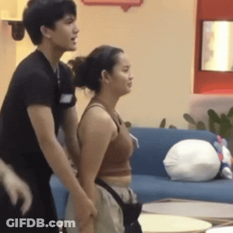 A Man And A Woman Are Standing Next To Each Other In Front Of A Blue Couch GIF