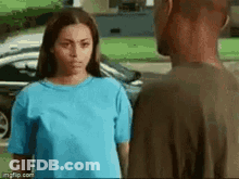 A Man And A Woman Are Standing Next To Each Other In Front Of A Car . The Woman Is Wearing A Blue Shirt . GIF