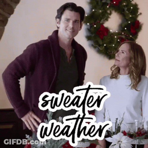 A Man And A Woman Are Standing Next To Each Other In Front Of A Christmas Wreath With The Words Sweater Weather Written GIF
