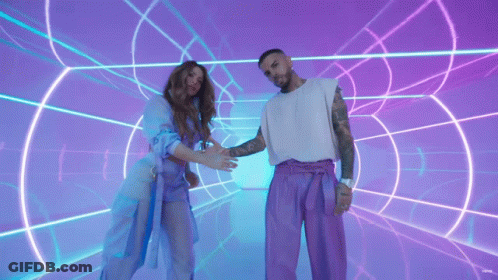 A Man And A Woman Are Standing Next To Each Other In Front Of A Neon Tunnel GIF