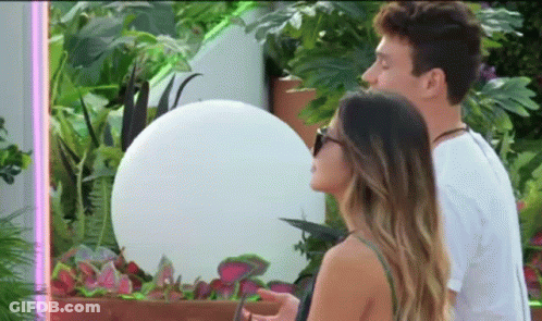 A Man And A Woman Are Standing Next To Each Other In Front Of A Plant . GIF