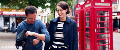 A Man And A Woman Are Standing Next To Each Other In Front Of A Red Phone Booth . GIF
