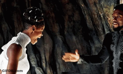 A Man And A Woman Are Standing Next To Each Other In Front Of A Rock Wall . GIF