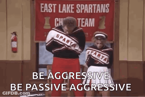 A Man And A Woman Are Standing Next To Each Other In Front Of A Sign That Says East Lake Spartans Cheer Team . GIF